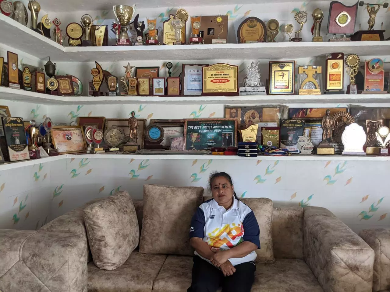 अपने घर में बैंठी पूनम। पीछे खेल के बदले उन्हें मिले सैंकड़ों ईनाम रखे हैं।