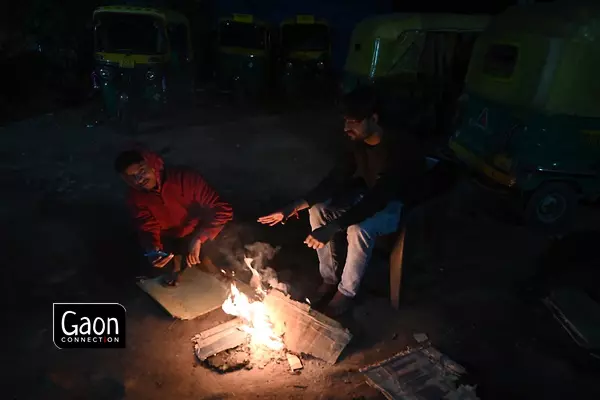 As seen in this photograph, two autorickshaw drivers are seen basking in heat from a small fire that they have arranged at their auto-stand. As seen in this photograph, two autorickshaw drivers are seen basking in heat from a small fire that they have arranged at their auto-stand.